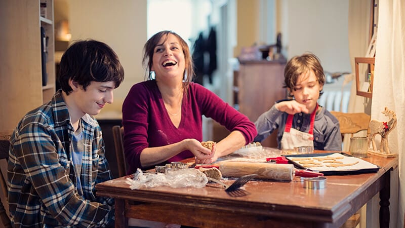 A mother and two boys making cookies at the table.