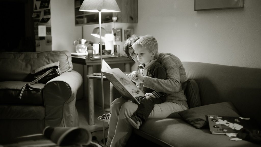 Little boy sitting on his parent's lap and reading a book together.