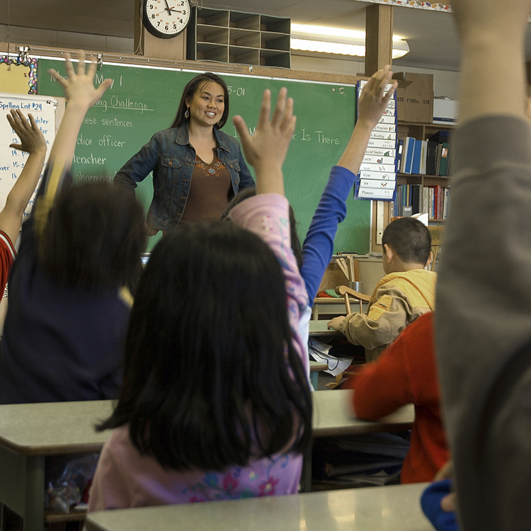 Teacher standing in front of classroom with children raising hands