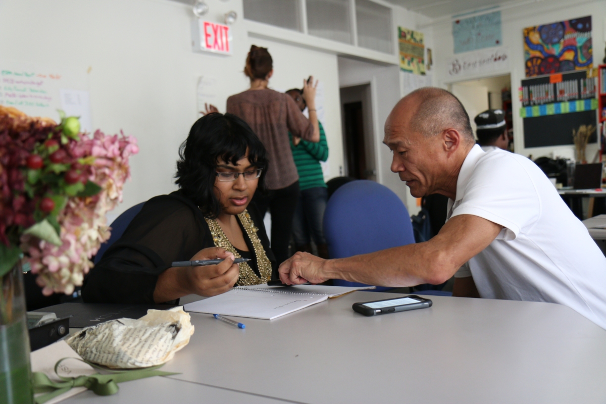 A woman with pen in hand and a man pointing at the notebook, seated at a table