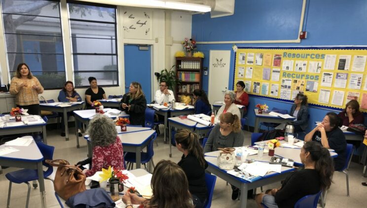 A group of parents sitting at children's desk in the classroom