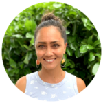 Photo of smiling woman in white top, in front of green hedges.