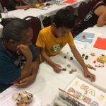 A grandmother and grandchild look at and sort kukui nuts by color on the table