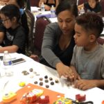 A mom and her son sit at the table looking at kukui nuts on the table